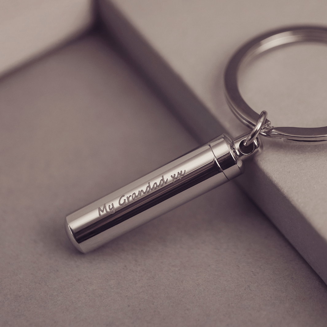 Cylindrical keyring which unscrews to hold cremation ashes or hair, engraved with the message "My Grandad xx" on one line, on a light grey background.