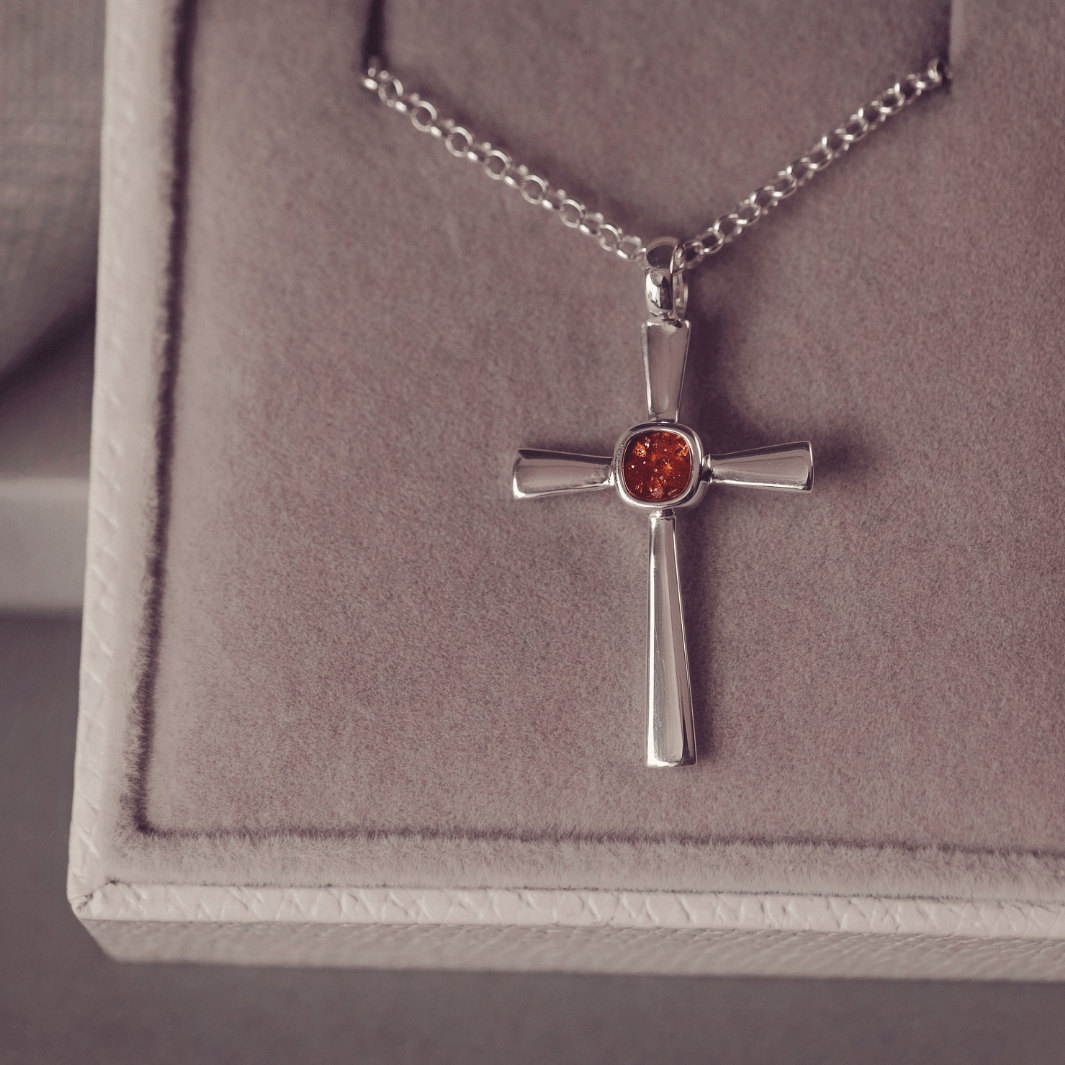 silver cross necklace with a section of resin and orange crystals, holding memorial ashes
