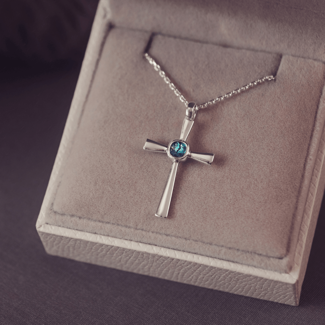 silver cross necklace with a section of resin and turquoise crystals, holding memorial ashes