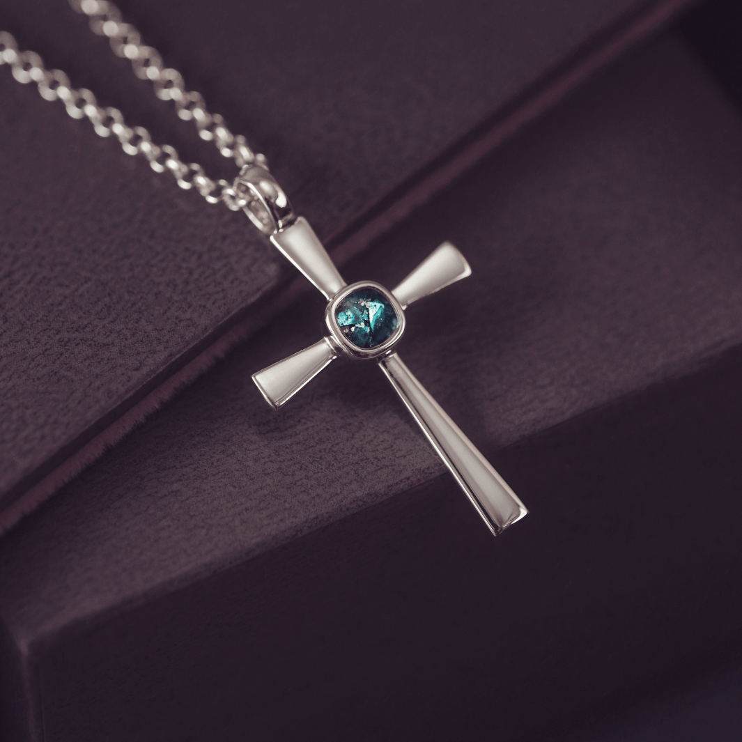 silver cross necklace with a section of resin and turquoise crystals, holding memorial ashes