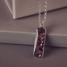 A sophisticated silver necklace featuring a rectangular pendant filled with shimmering brown crystal and resin, delicately layered with cremation ashes, showcased against a dark background, on a silver belcher chain.
