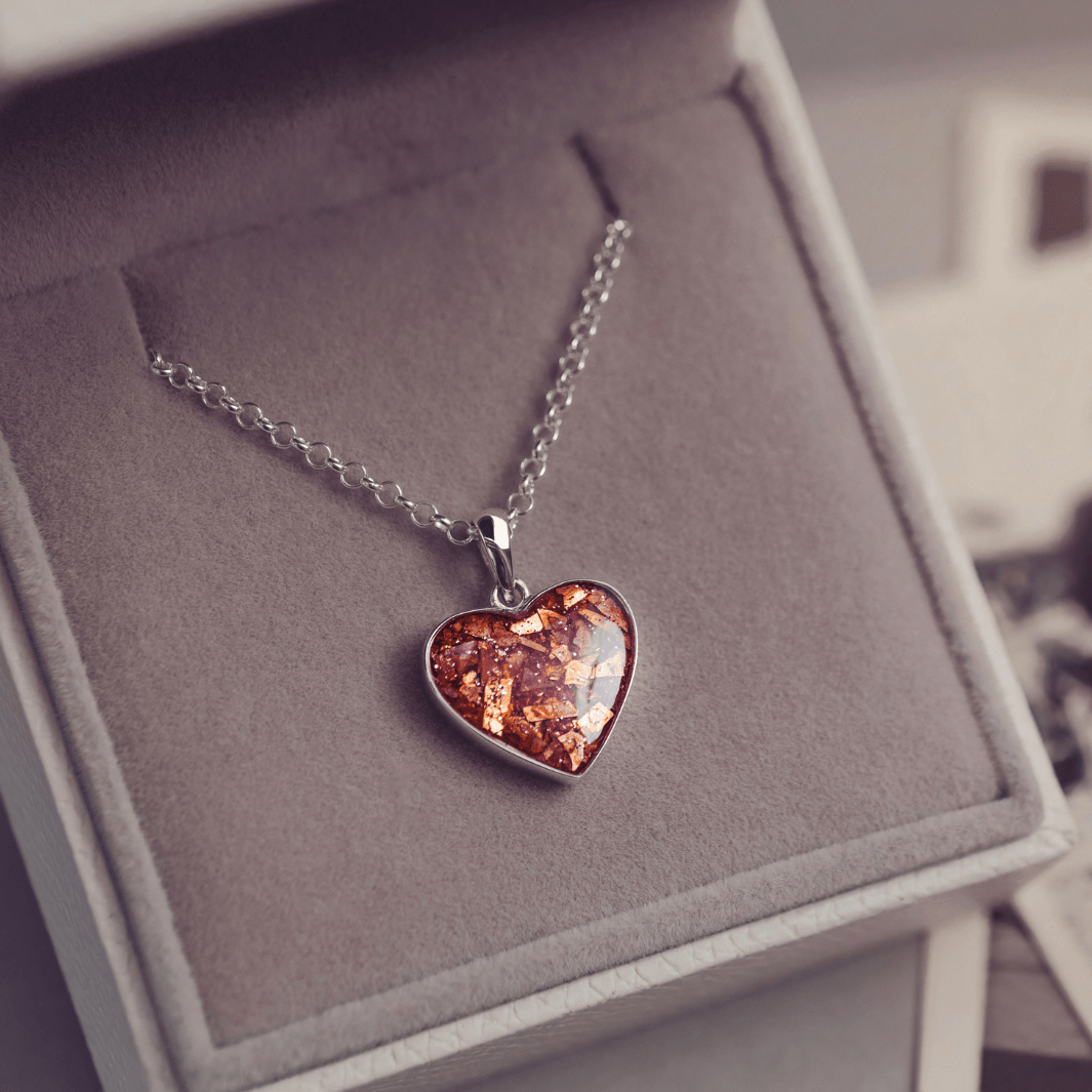 Sterling silver heart necklace with a central section filled with memorial ashes and orange crushed crystals, displayed in a grey jewellery box