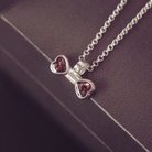 A silver chain necklace with a bow-shaped pendant featuring two heart-shaped brown gemstone inlays, displayed on a dark textured surface.