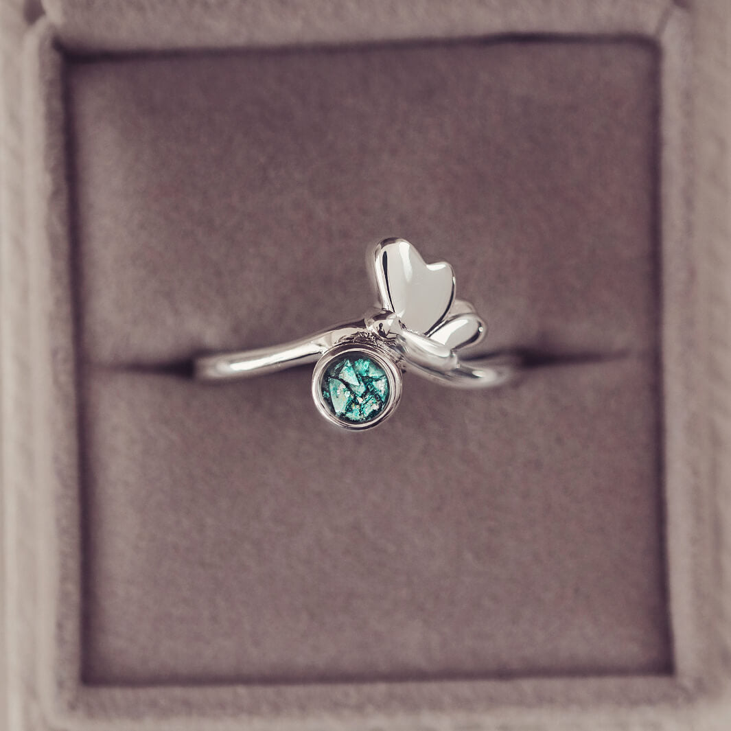 Silver butterfly ring, with green crystals and cremation ashes. In a grey jewellery box.