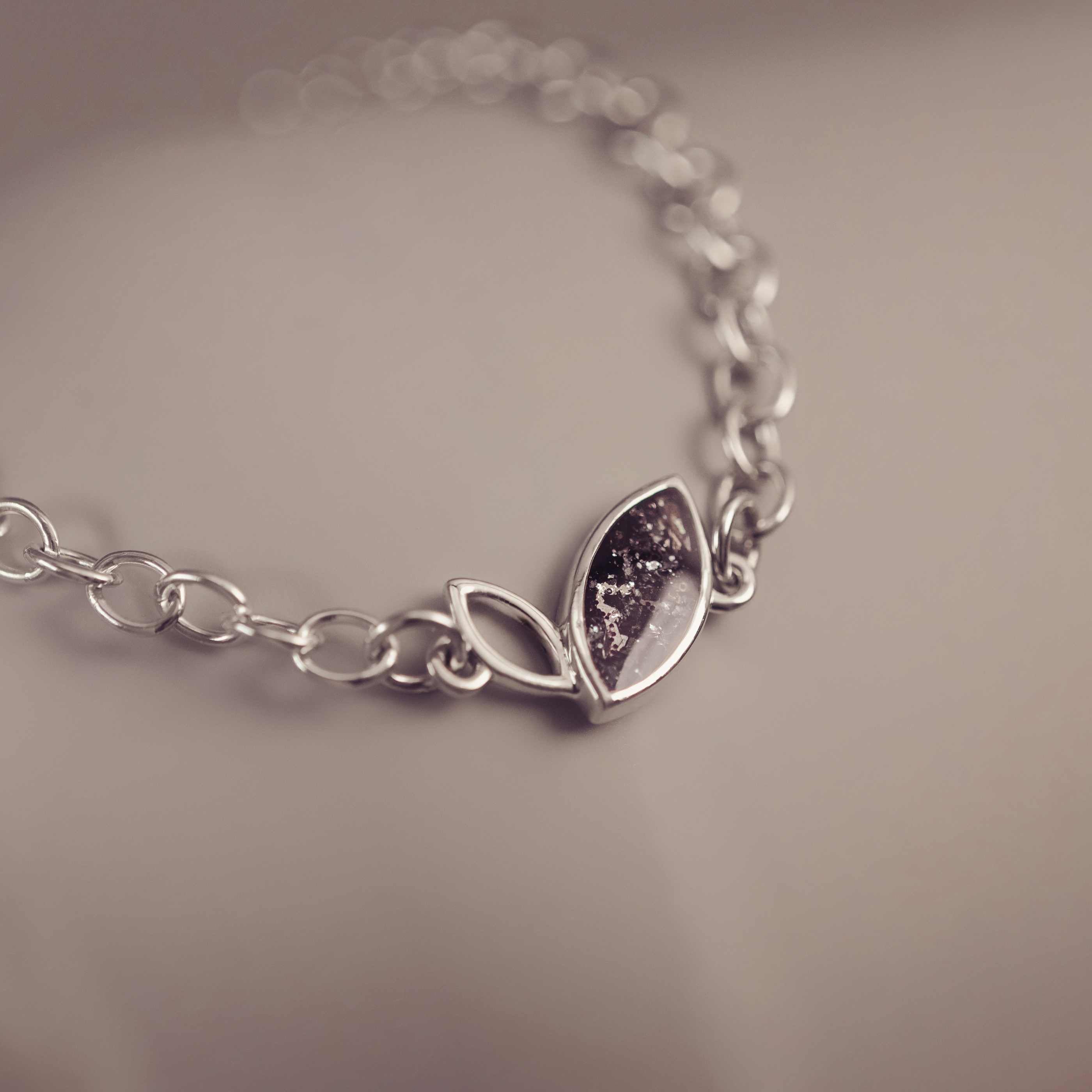 Silver bracelet with a leaf-shaped charm on a neutral background