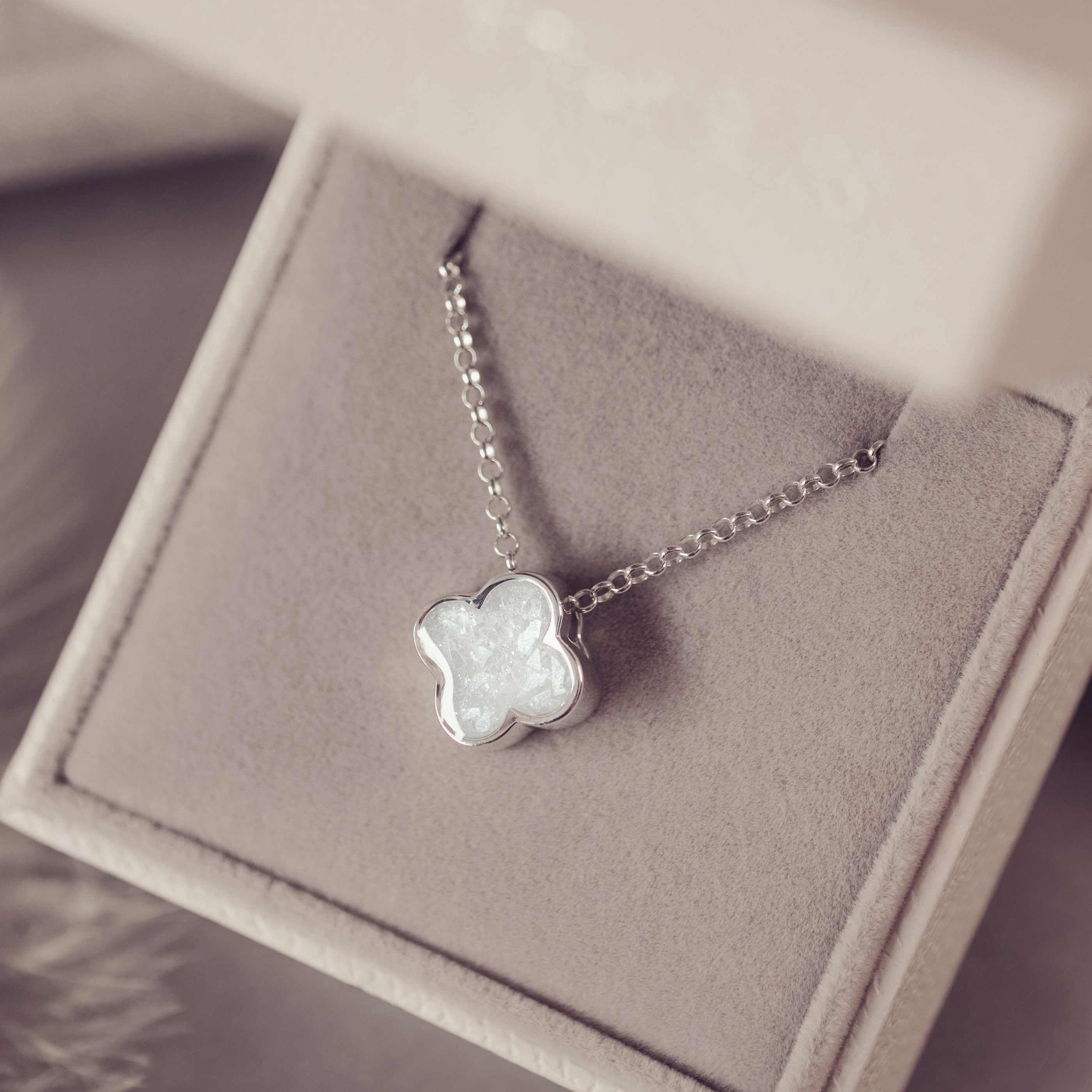 Silver necklace with a white clover-shaped pendant on a soft purple background
