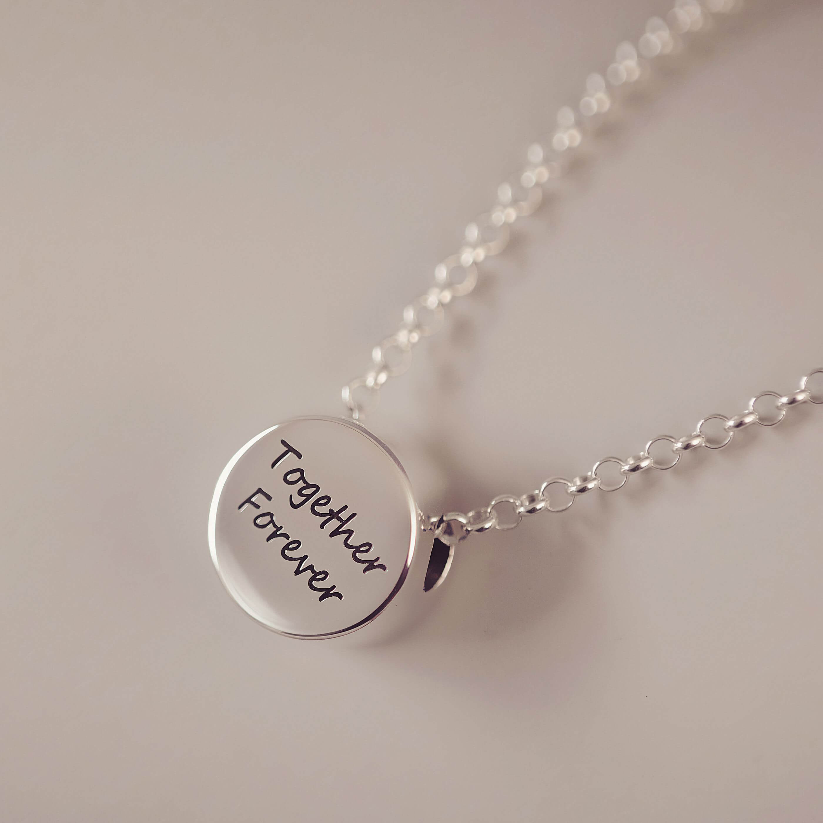 Silver necklace with a round pendant inscribed 'Together Forever' on a light background