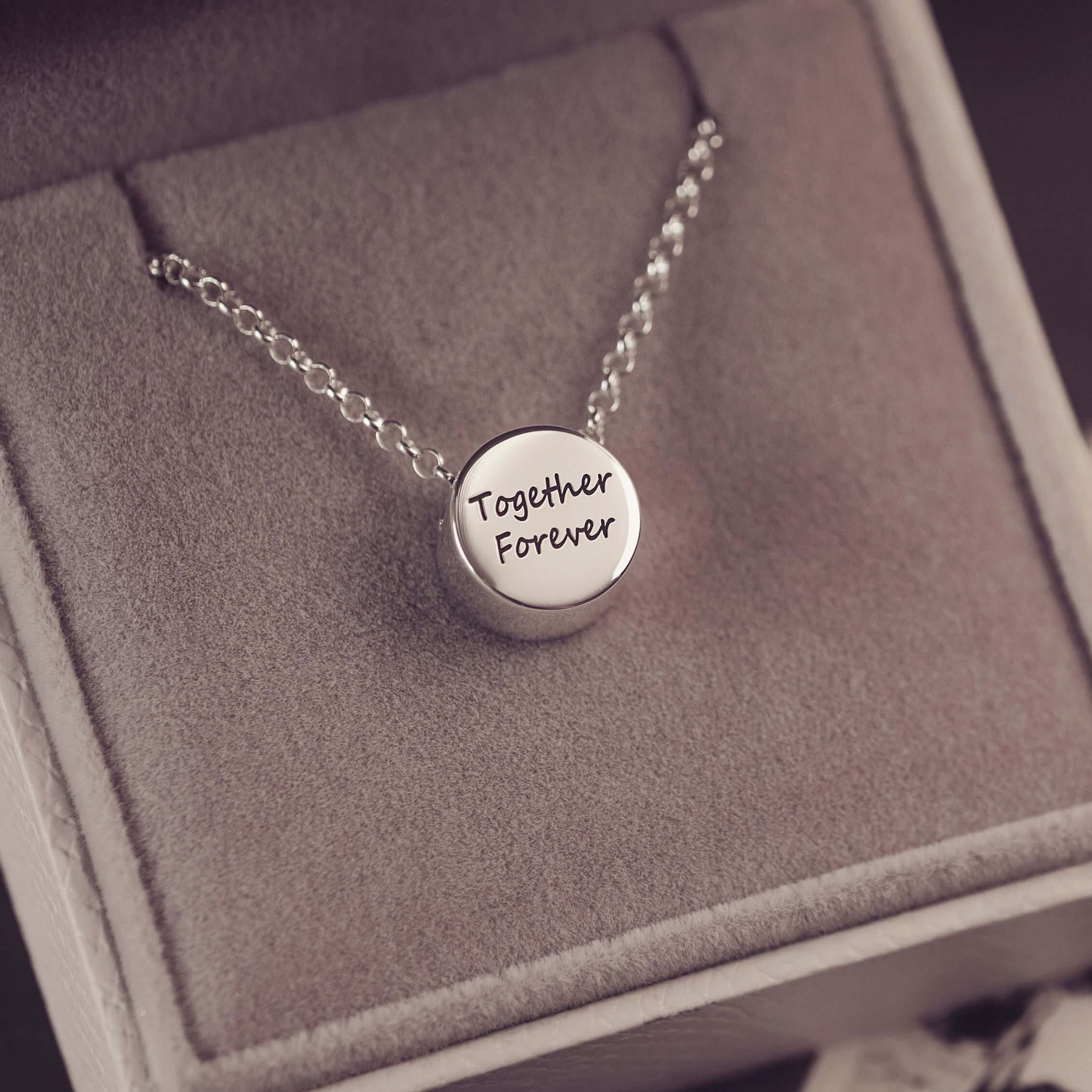 Silver necklace with 'Together Forever' pendant on a gray box