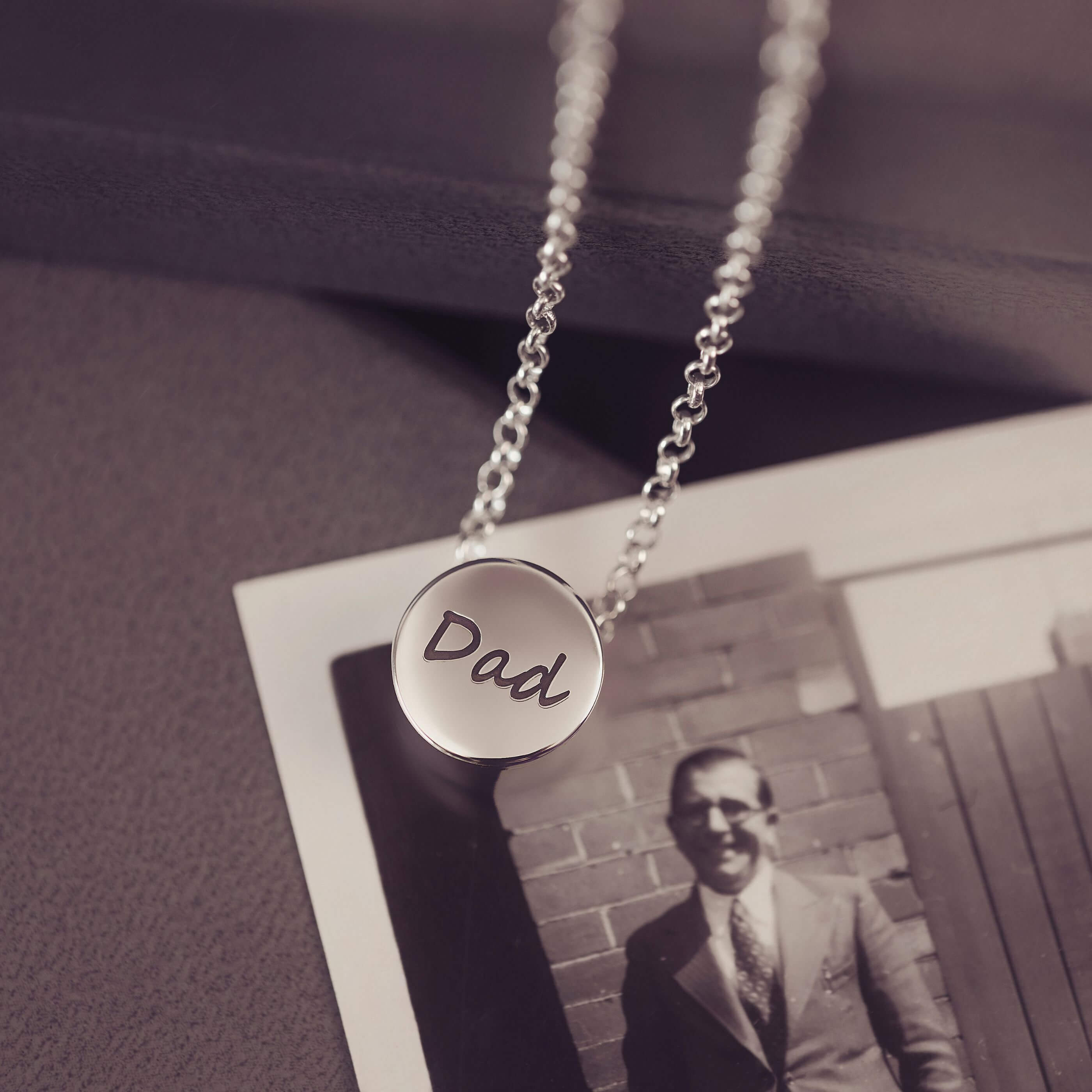 Silver necklace with 'Dad' pendant on a vintage photo background
