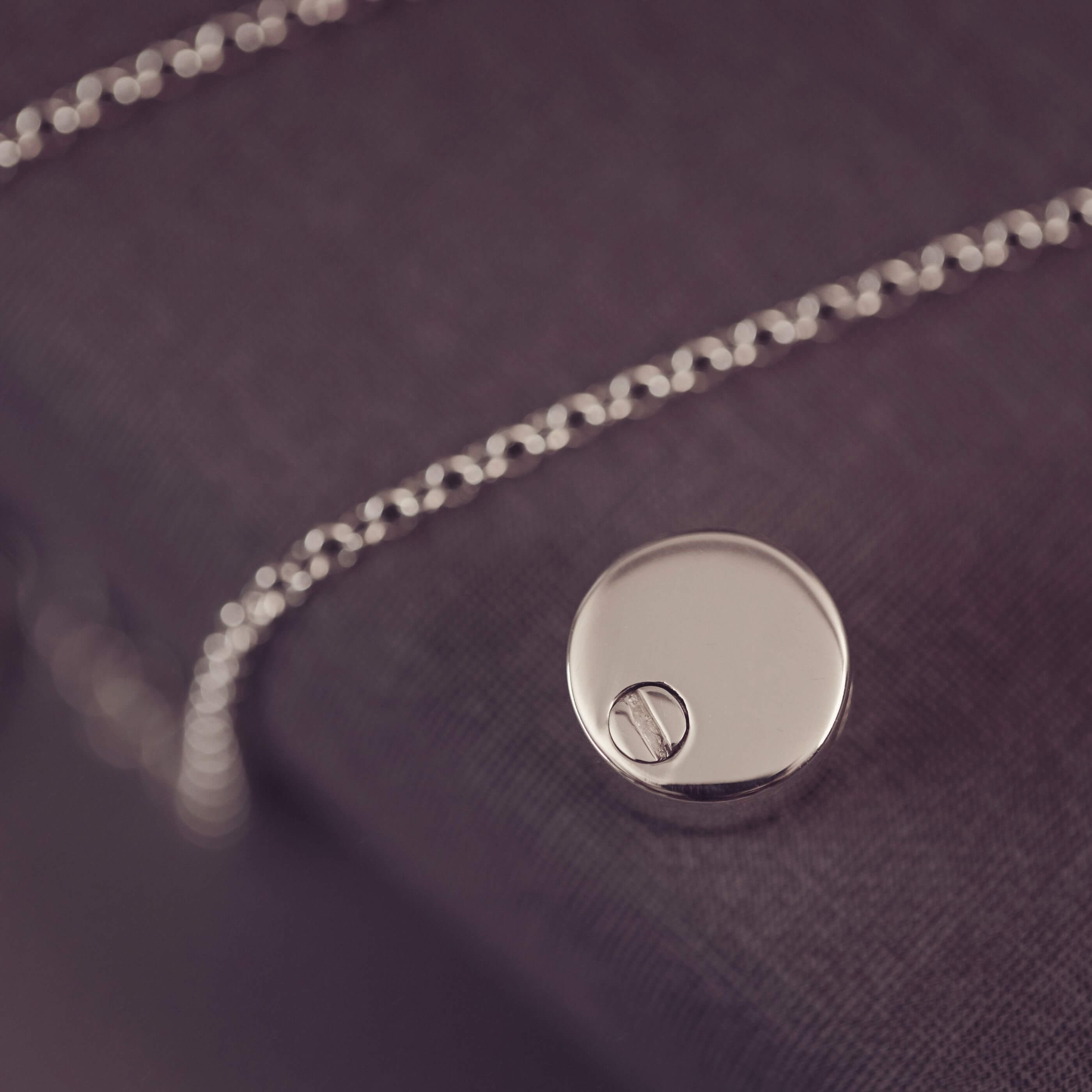 Close-up of a silver necklace with a round pendant on a dark fabric background
