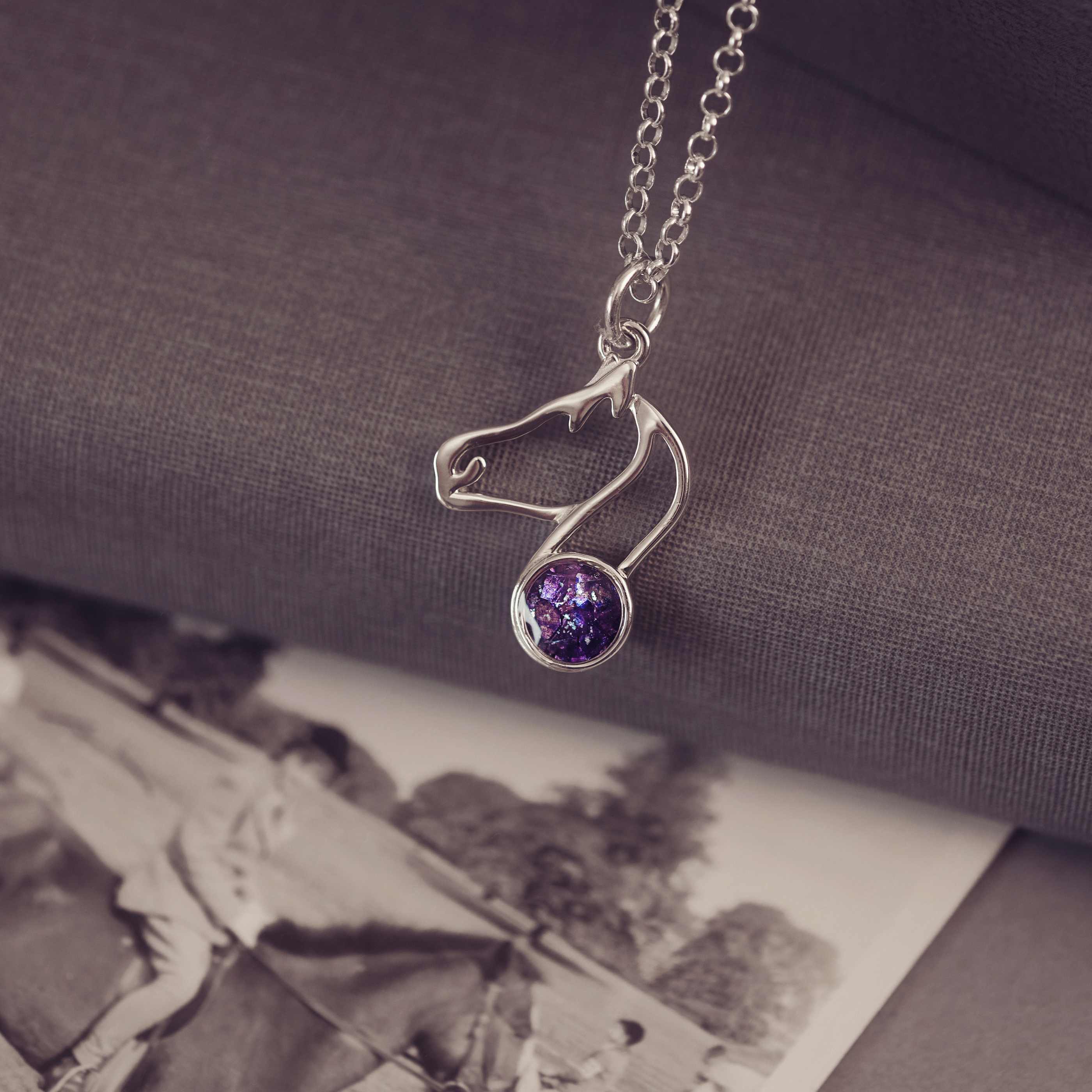 Silver necklace with a purple gemstone pendant on a textured surface with an old photograph underneath.