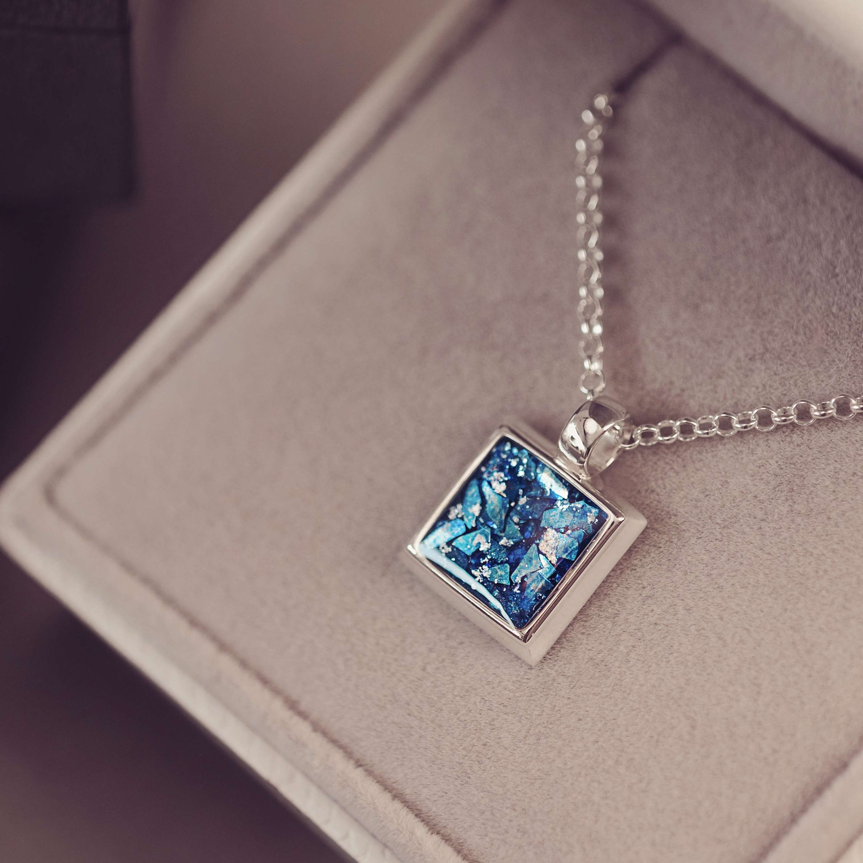A silver square necklace filled with clue ashes and gemstones