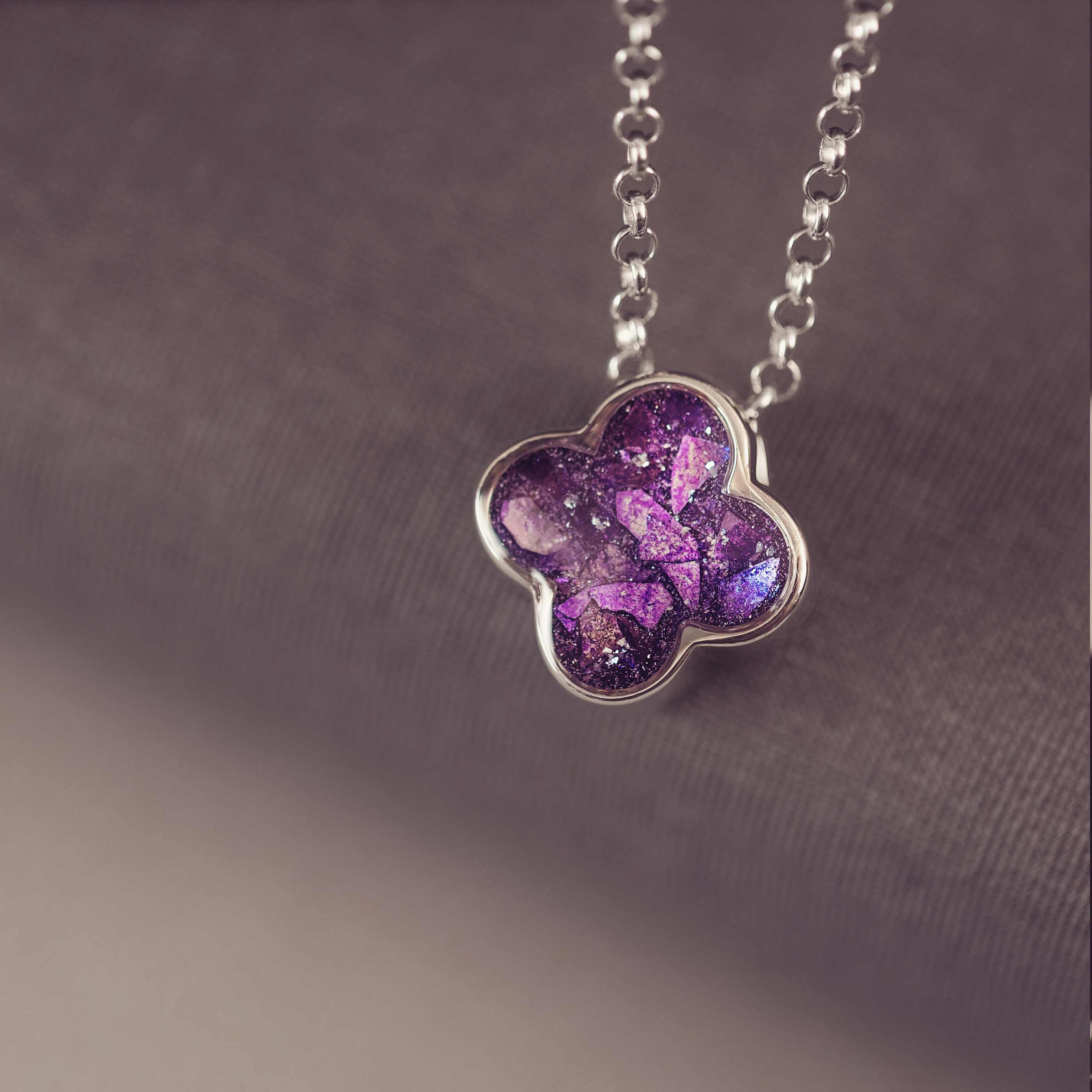Purple flower-shaped pendant on a chain against a dark background