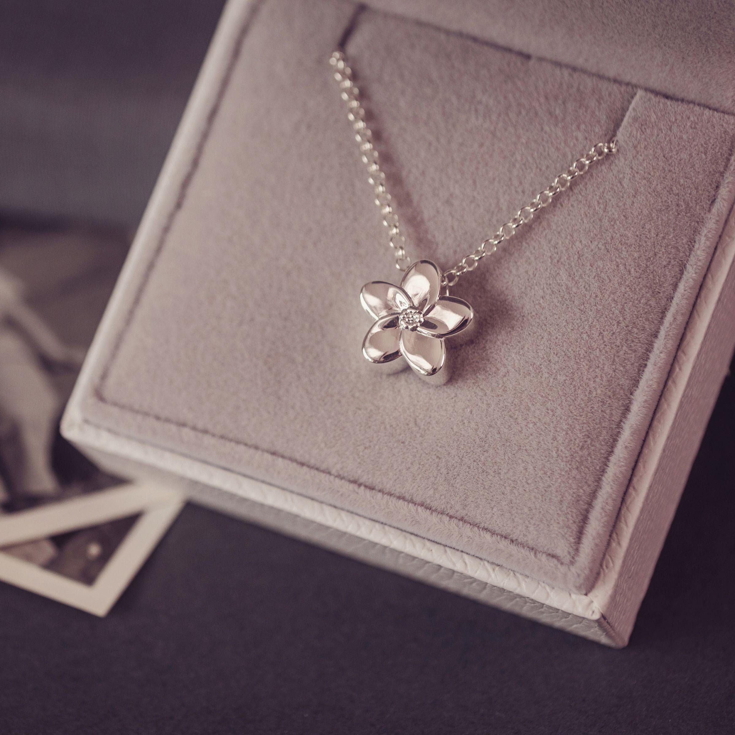 A silver flower pendant necklace resting on a gray velvet jewelry box.
