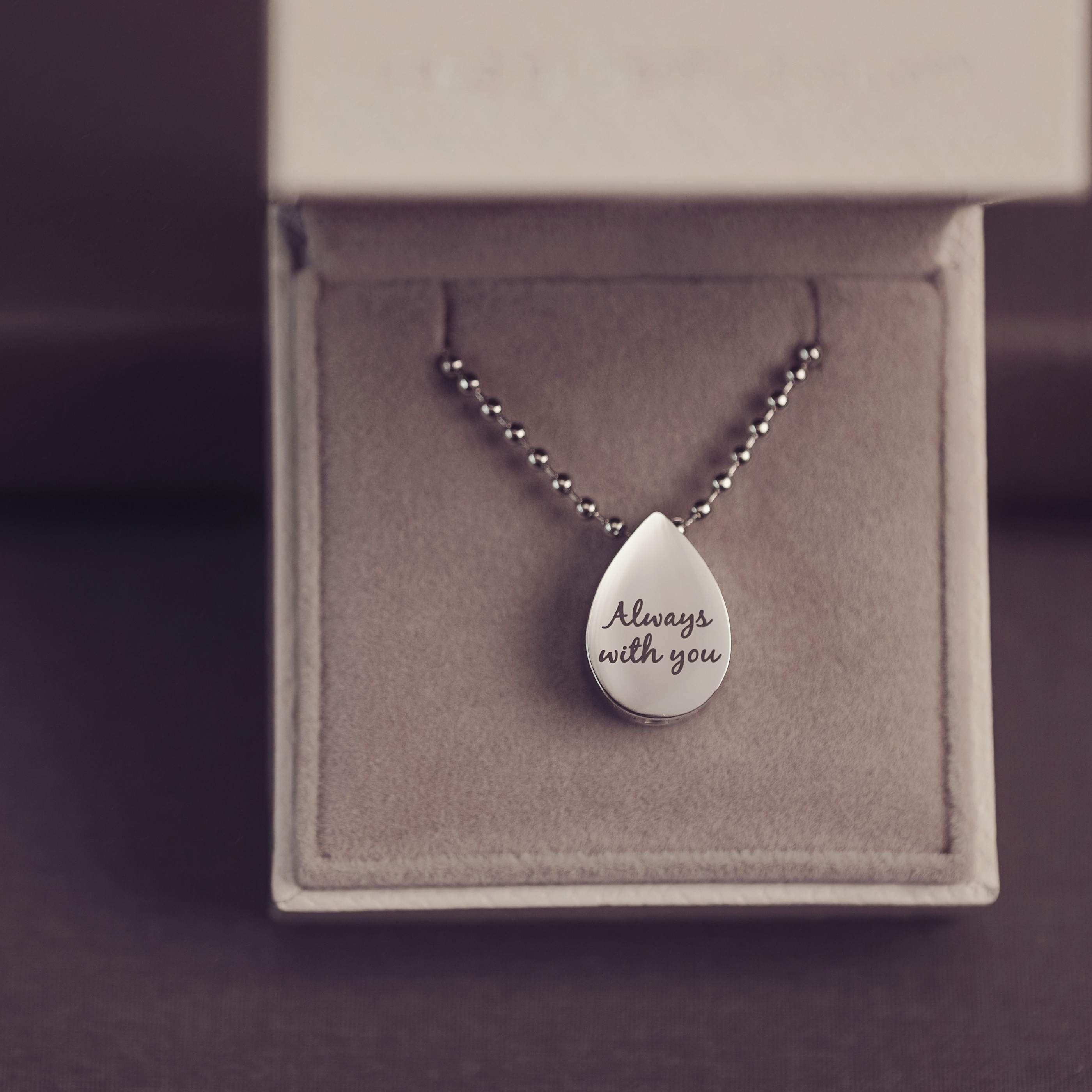 Silver teardrop pendant necklace with 'Always with you' engraving on a gray box.