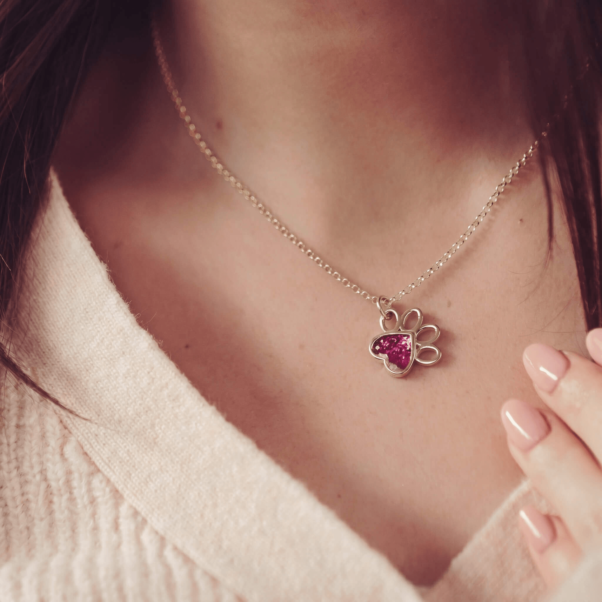 Woman in a jumper wearing a gold pawprint shaped necklace, with pink gem setting