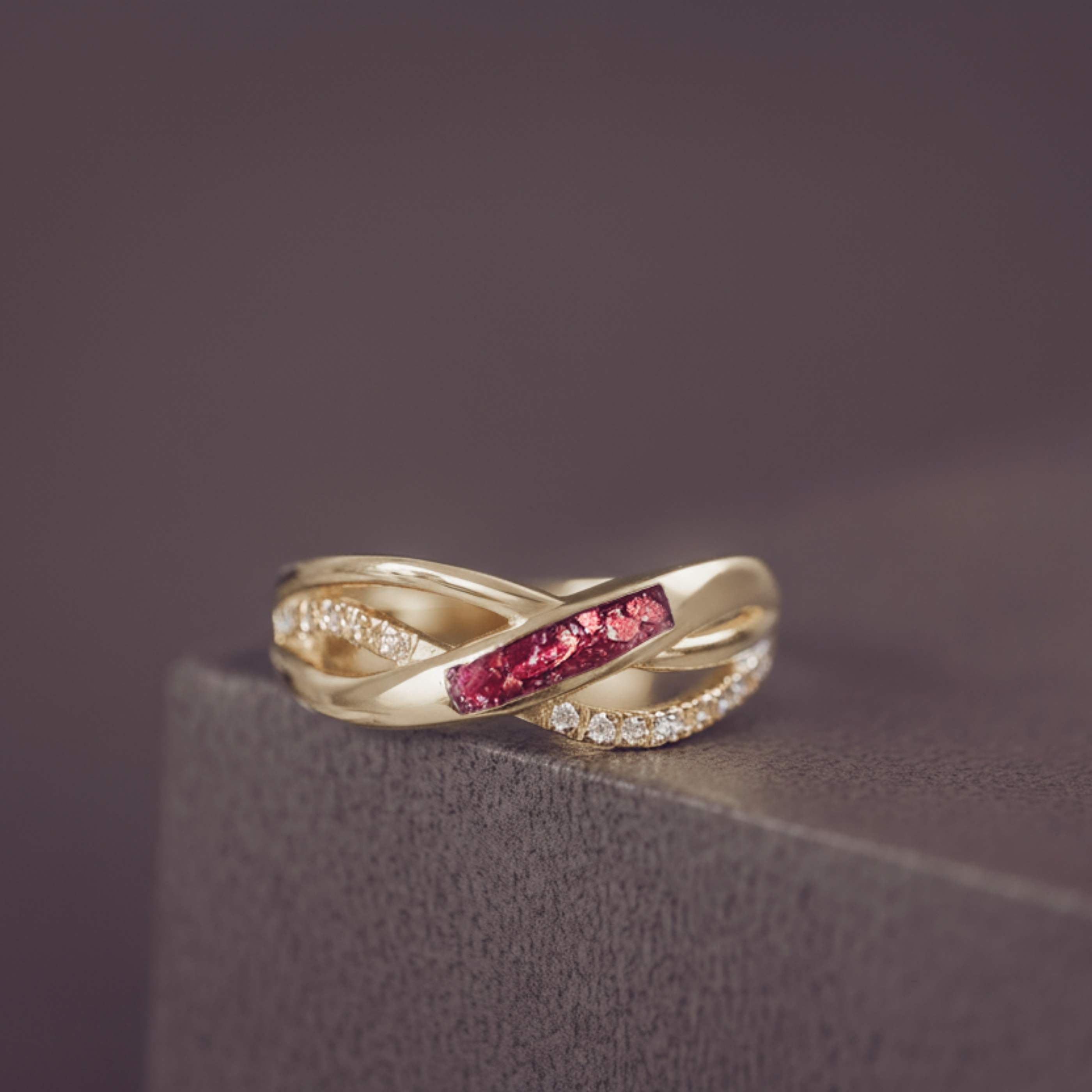 Gold ring with red gemstone and diamond accents on a dark surface