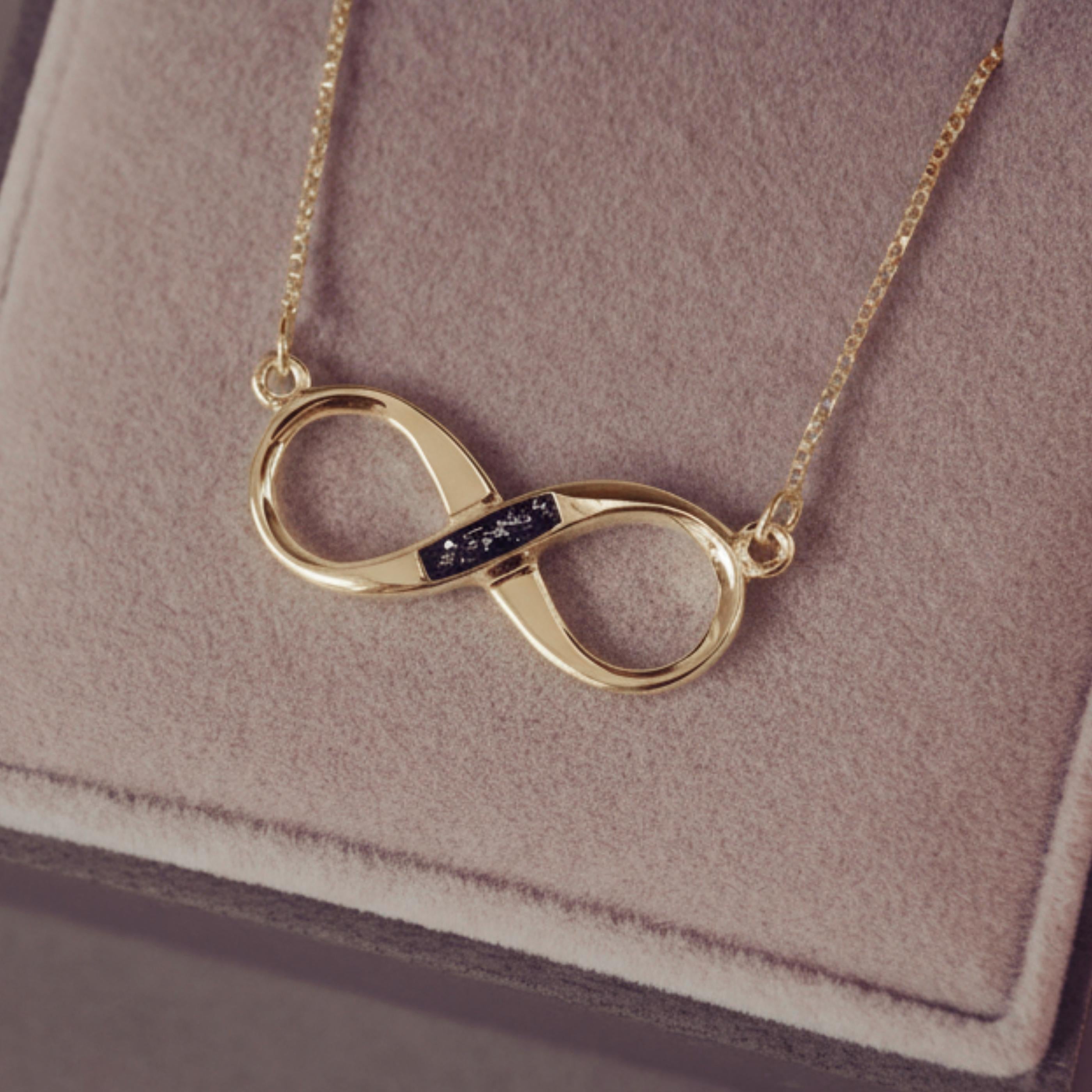 Gold infinity necklace on a soft pink background