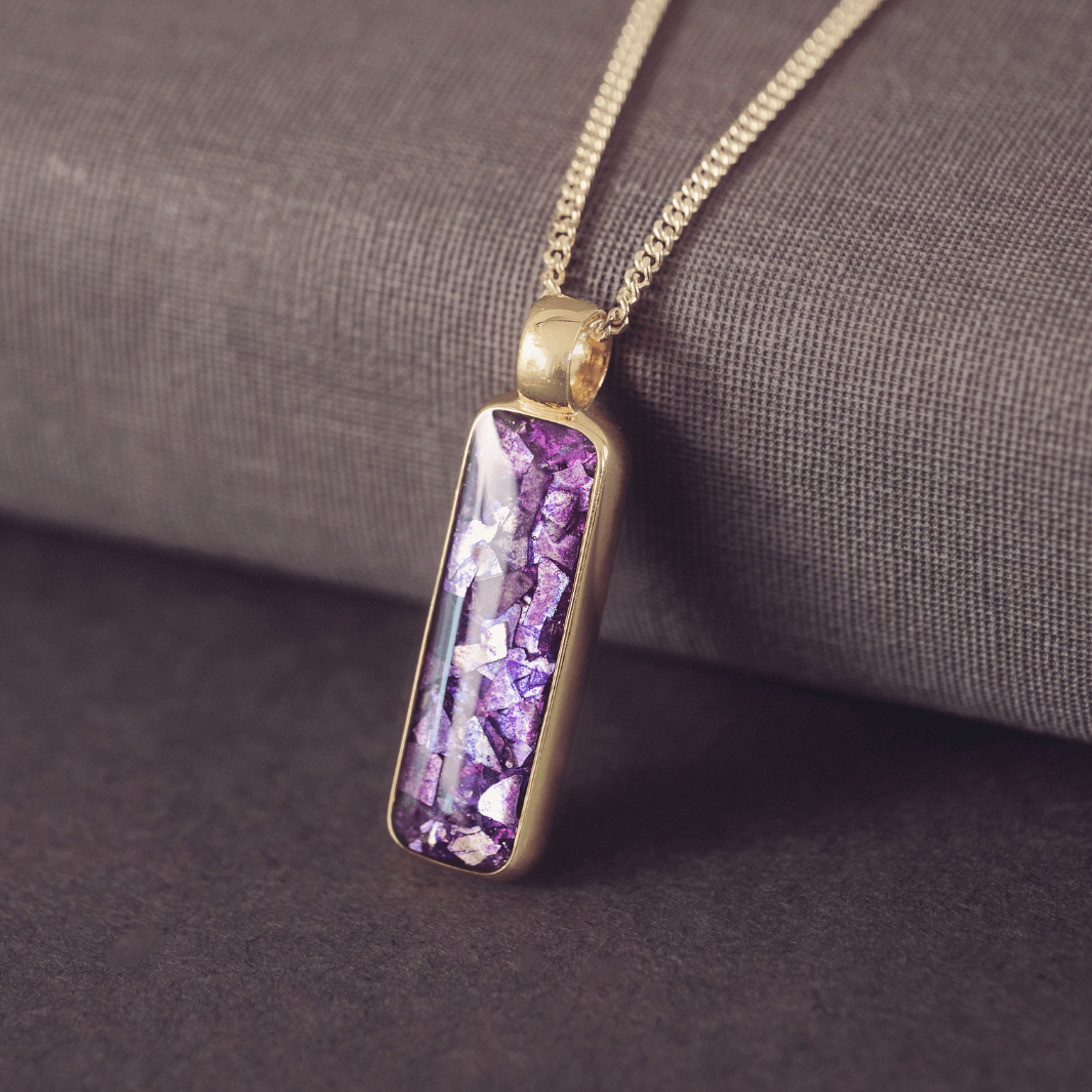 Gold necklace with a purple pendant on a textured surface