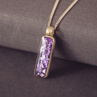 Gold necklace with a purple pendant on a textured surface