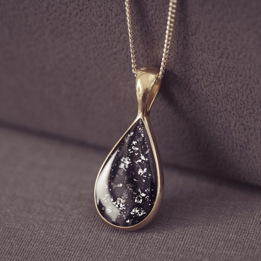 Teardrop-shaped pendant crafted in 9 carat gold on a dark fabric background
