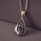 Teardrop-shaped pendant crafted in 9 carat gold on a dark fabric background