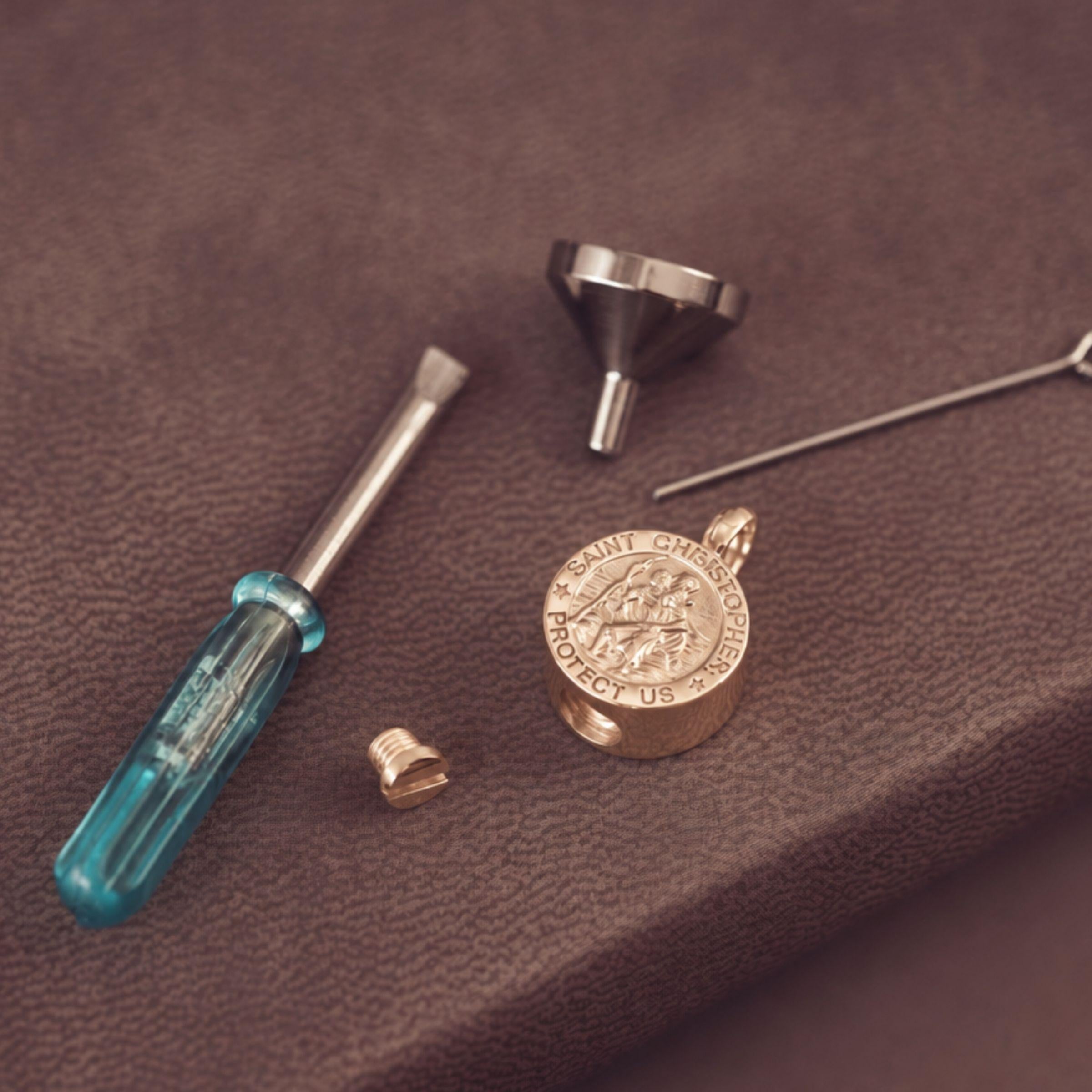 A small set of jewellery tools with a blue-handled screwdriver, metal funnel, small screw piece, and thin pin, arranged on a brown textured surface.