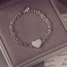 Silver chain bracelet with a heart-shaped charm on a soft surface