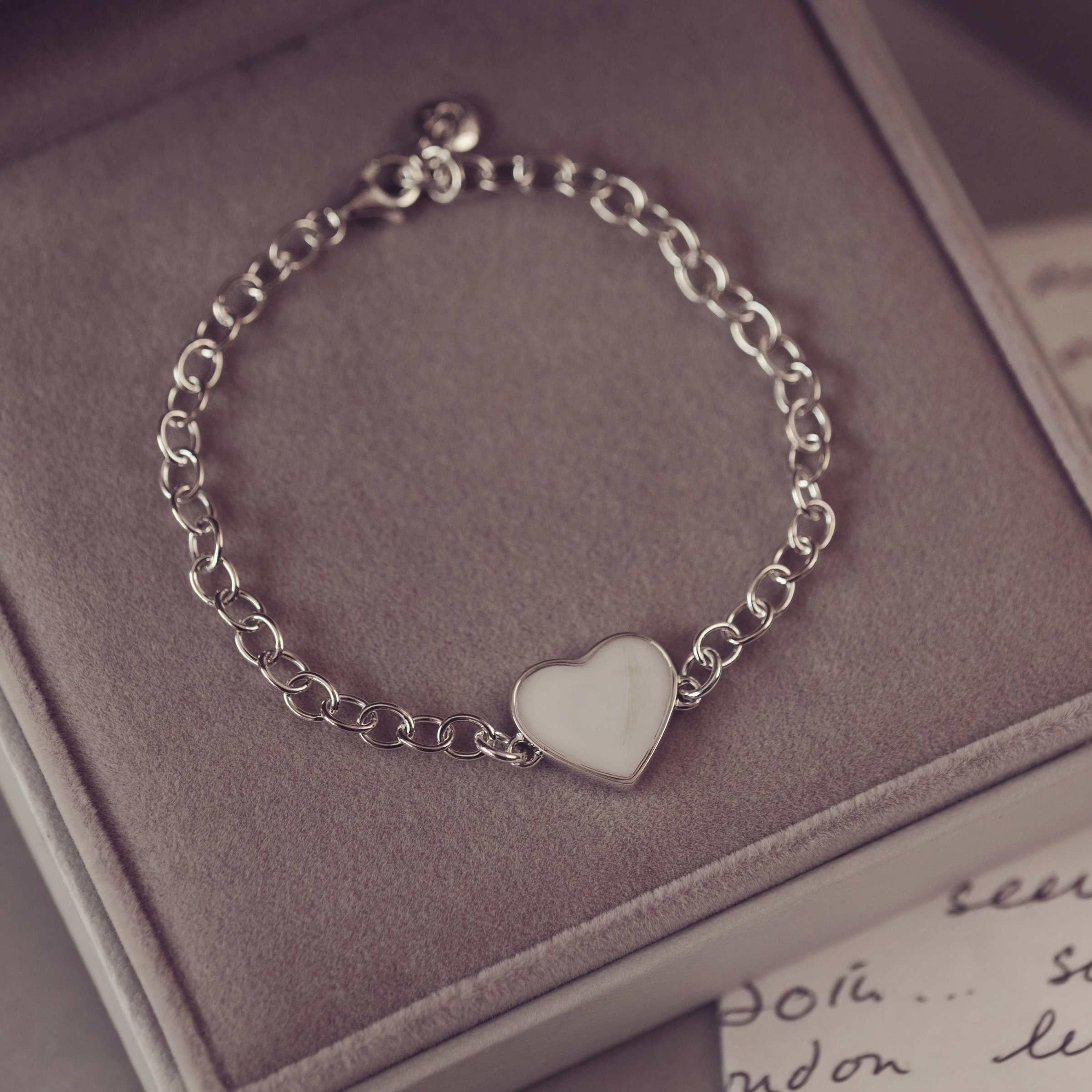 Silver chain bracelet with a heart-shaped charm on a soft surface