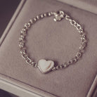 Silver bracelet with a heart-shaped charm on a soft surface