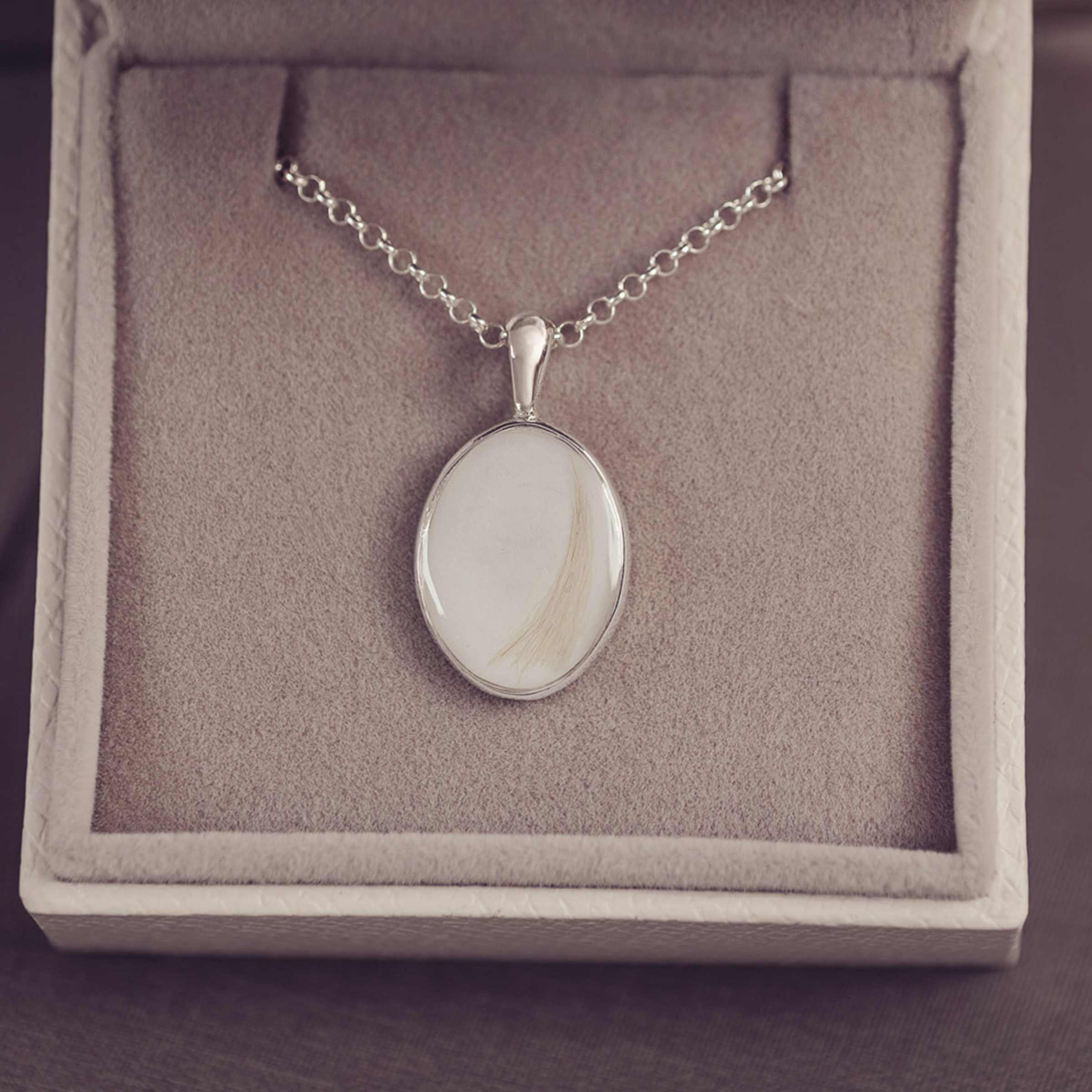 Silver necklace with a pendant on a gray cushioned jewelry box