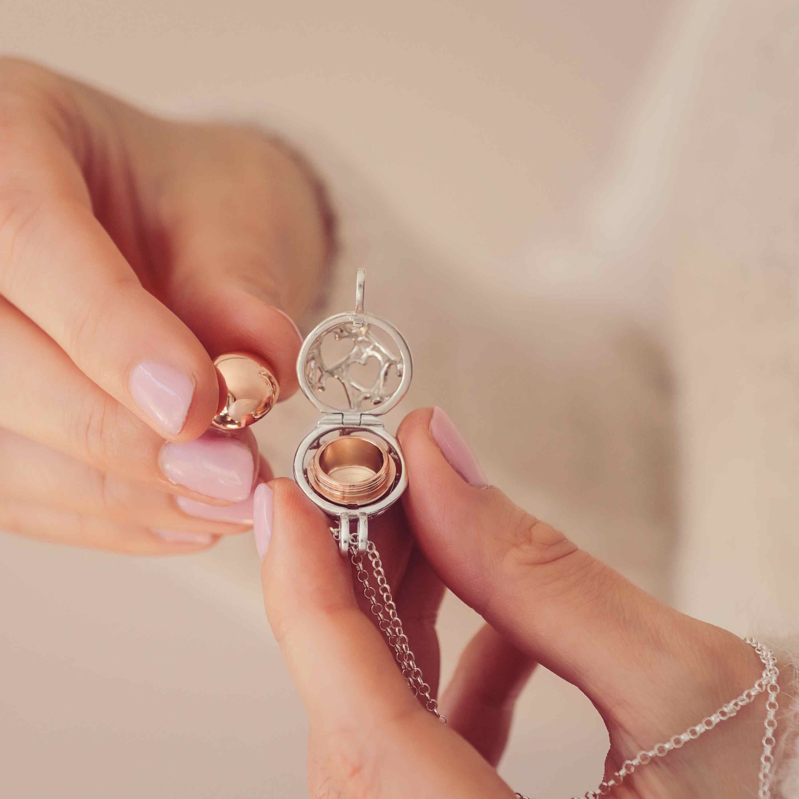 A Silver and gold round locket with the word Mum engraved held in a ladies hands
