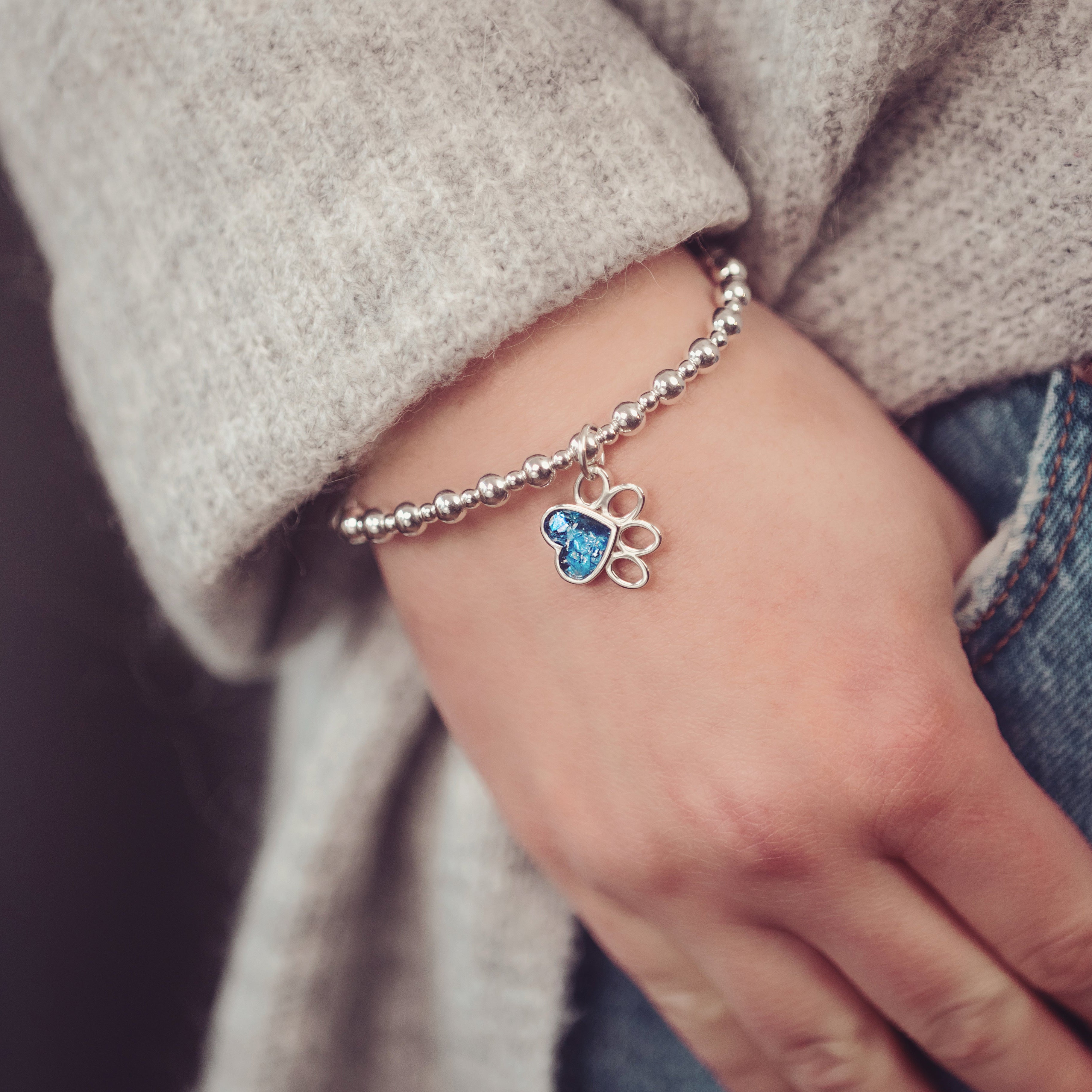 silver bead bracelet, worn on a wrist, with a paw print memorial ashes charm