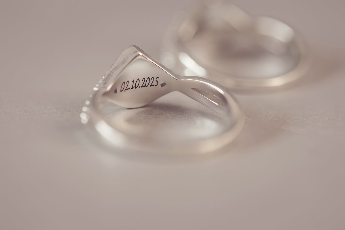 A close-up of a polished silver ring with a triangular top engraved with the date 02.10.2025