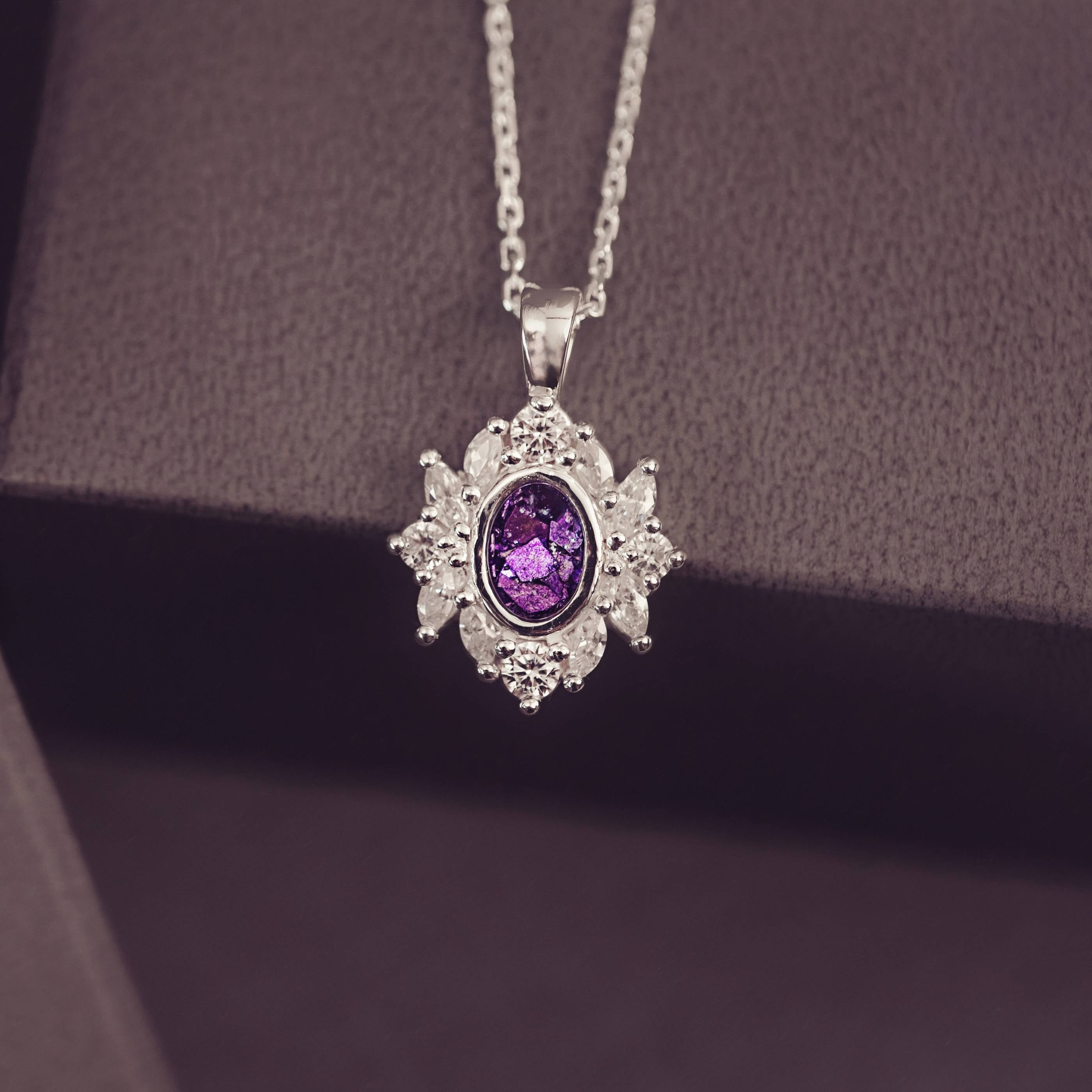 Silver pendant with a purple gemstone on a chain against a dark background