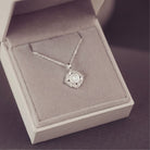 Silver necklace with a pendant in an open jewelry box on a purple background