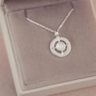 Silver necklace with a circular pendant on a pink jewelry box