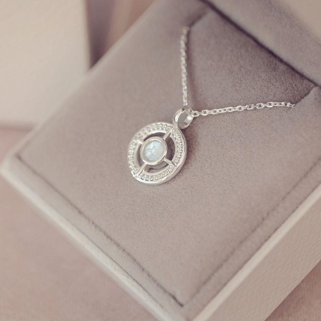 Silver necklace with a circular pendant on a soft pink surface