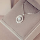Silver necklace with a circular pendant on a soft pink surface
