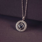 Silver necklace with a circular pendant on a dark purple background