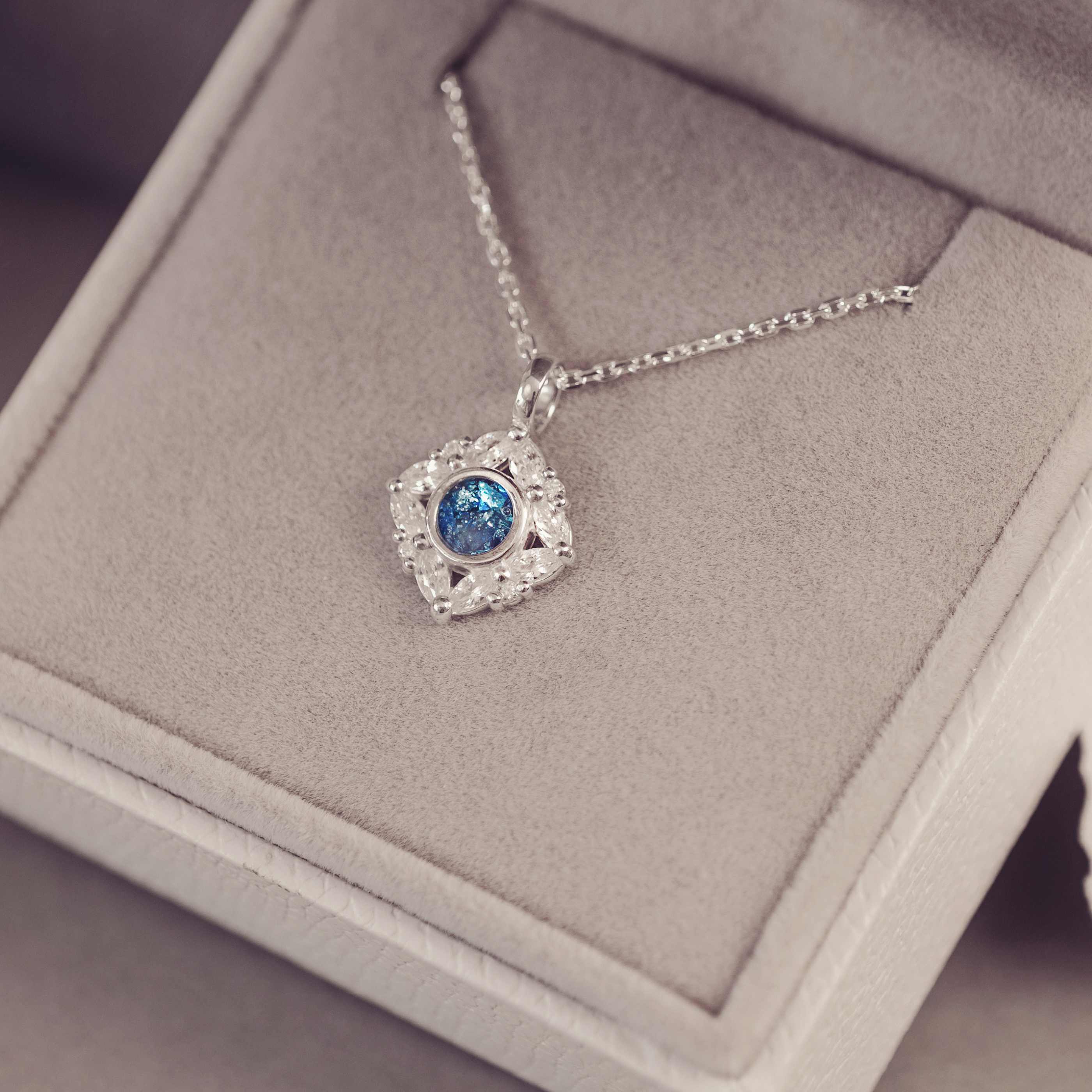 Silver necklace with a blue gemstone pendant on a gray cushion