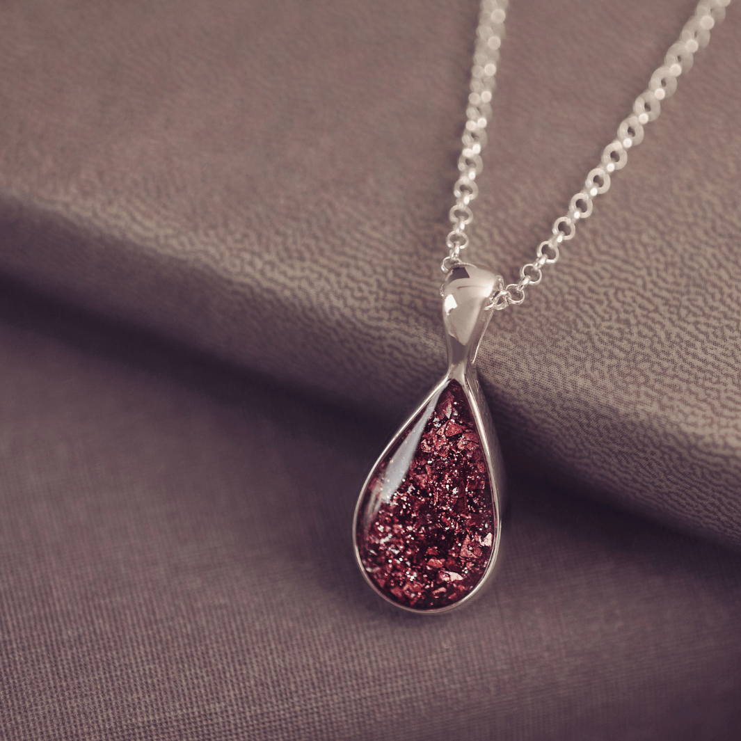 Sterling silver teardrop necklace with a central section filled with memorial ashes and brown crushed crystals, displayed on dark background
