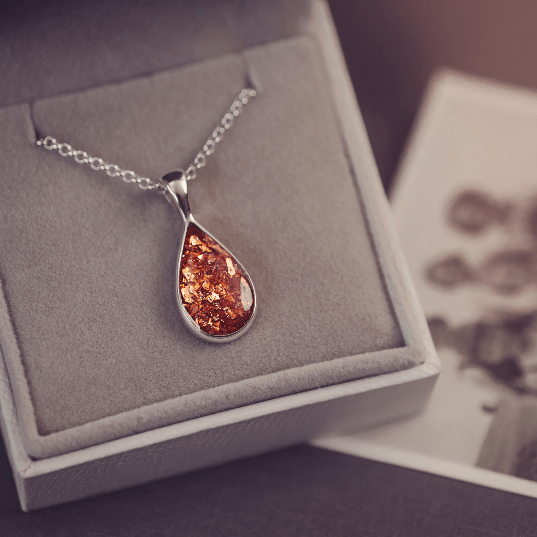Sterling silver teardrop necklace with a central section filled with memorial ashes and orange crushed crystals, displayed in a grey jewellery box