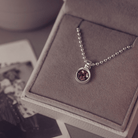A sophisticated Mens silver necklace featuring a small round pendant filled with shimmering brown crystal and resin, delicately layered with cremation ashes, showcased against a dark background on a silver ball chain