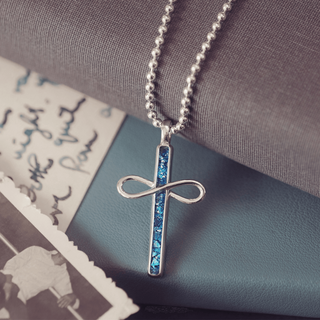 Silver cross pendant necklace with blue accents on a textured surface