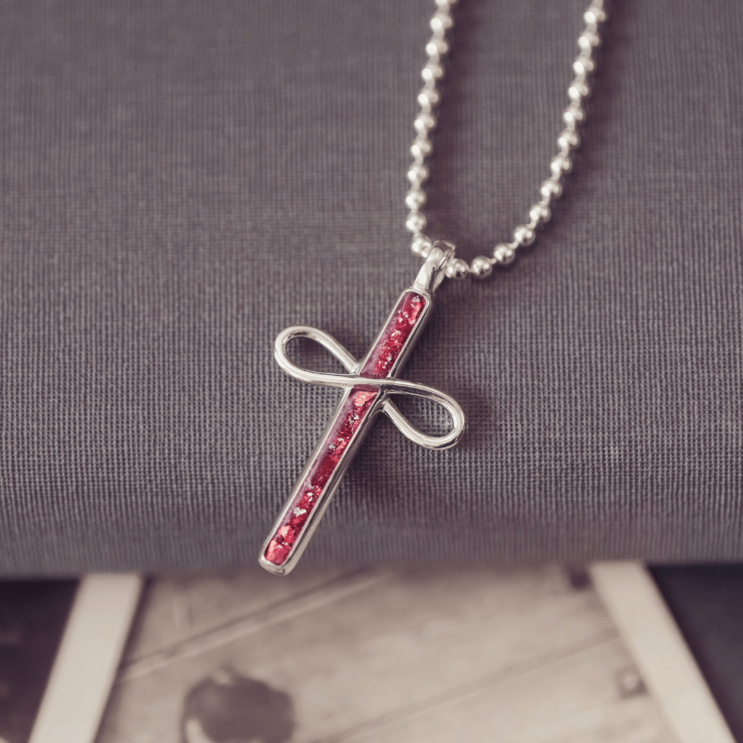 Silver cross pendant with red stones on a chain against a gray background