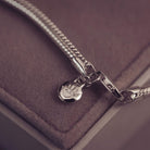 Silver chain necklace with paw print charm on a soft purple surface