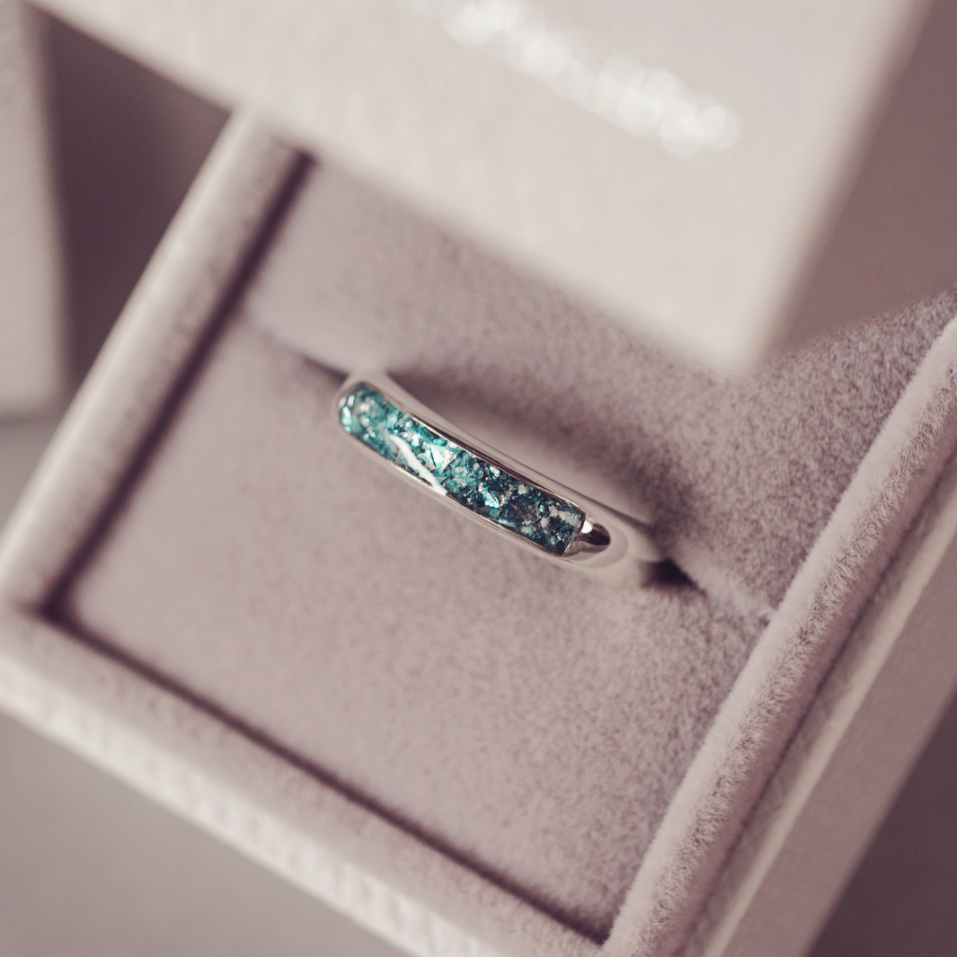 A silver band ring with a textured, crackled turquoise blue inlay, displayed inside an open light beige jewelry box.