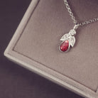Silver necklace with a red teardrop pendant on a gray surface