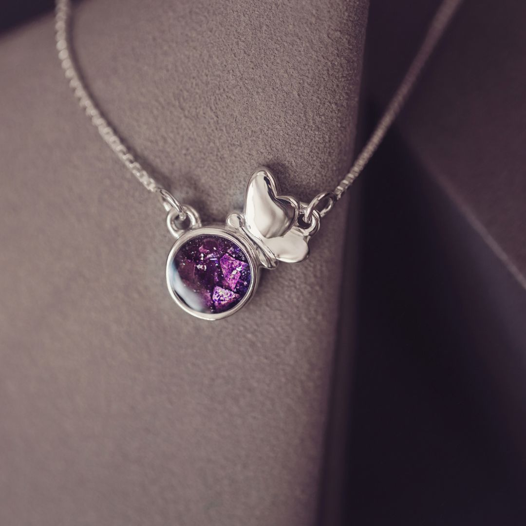 Necklace with a purple pendant and silver butterfly charm on a neutral background